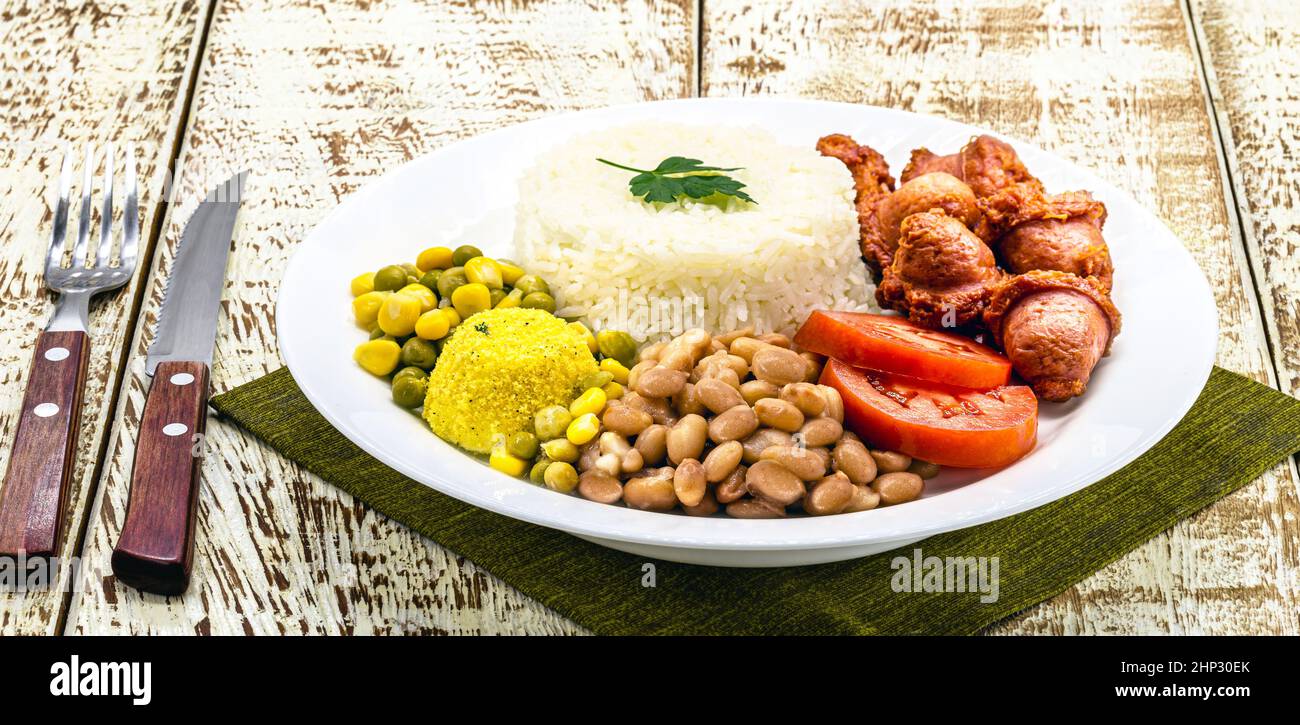 riso con fagioli brasiliani, servito con insalata, salsiccia fritta e farofa. Servito su un tavolo rustico Foto Stock