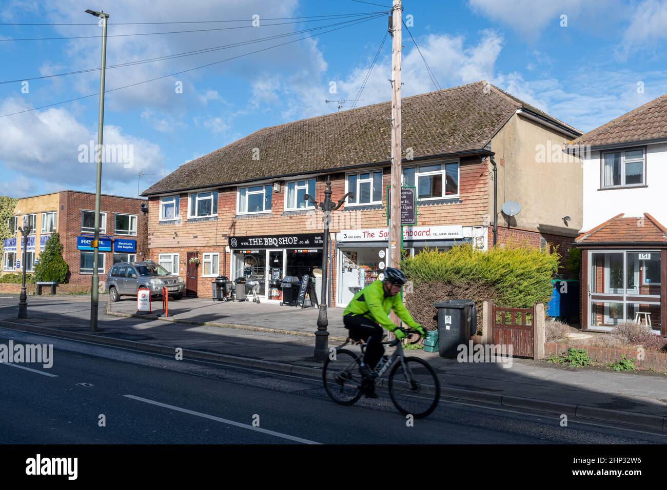 Ciclista che passa accanto a negozi e aziende sulla High Street nel villaggio Old Woking, Surrey, Inghilterra, Regno Unito Foto Stock