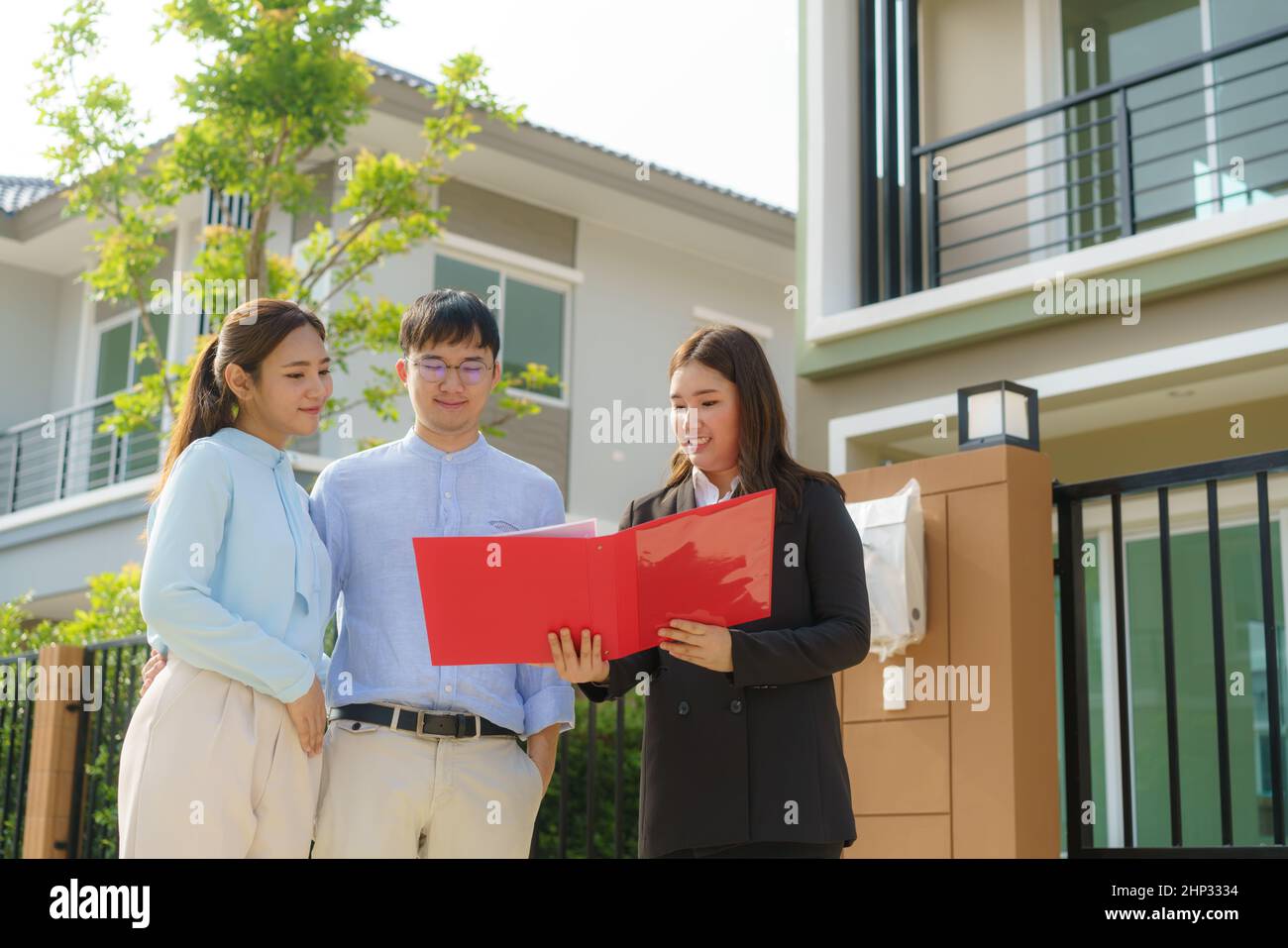 Donna asiatica Agente broker immobiliare che mostra un dettaglio della casa nel suo file per la giovane coppia asiatica amante cercando e interesse a comprarlo. Acquisto di una nuova ora Foto Stock
