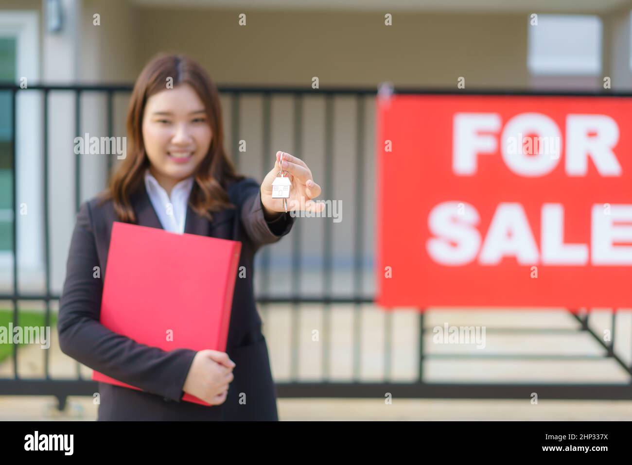 Agente immobiliare asiatico o donna immobiliare sorridente e tenendo file rosso con mostrare la chiave di casa di fronte alla casa. Foto Stock