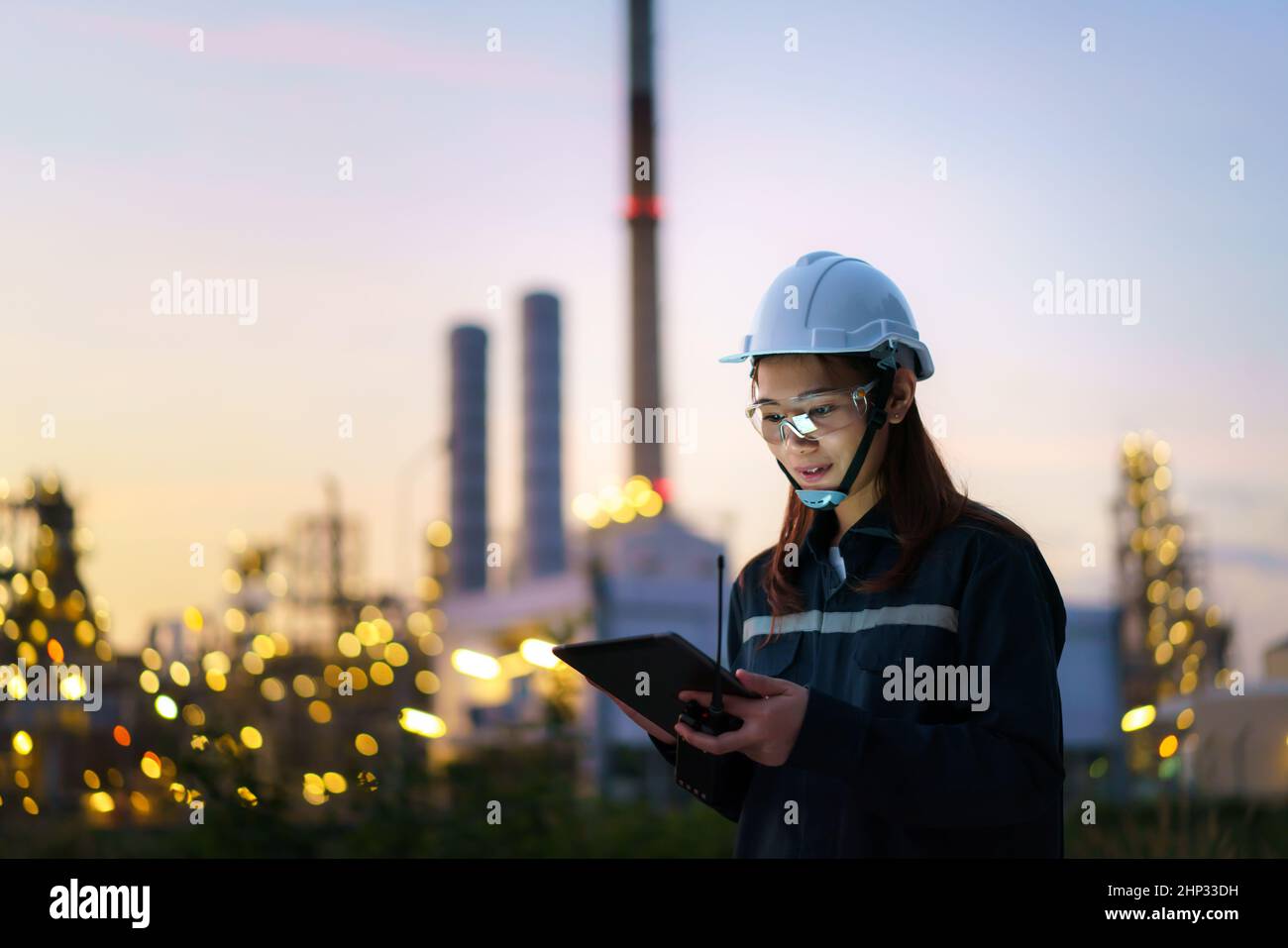 Donna asiatica ingegnere petrolchimico che lavora di notte con tablet digitale all'interno di petrolio e gas raffineria stabilimento di industria di notte per ispettore sicuro Foto Stock