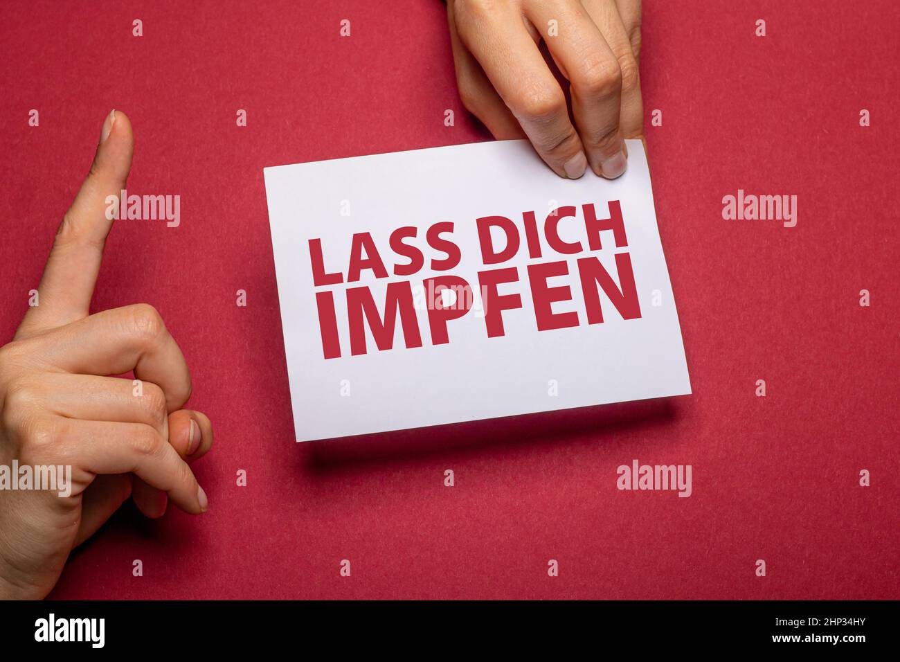 la mano femmina tiene un pezzo di carta con il testo lass dich impfen (ottenere vaccinato in lingua tedesca) davanti ad un cartone rosso scuro di fondo con Foto Stock