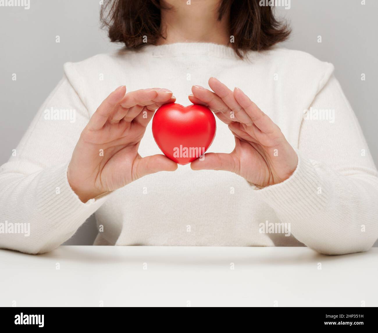 donna in un maglione bianco che tiene un cuore rosso, il concetto di amore e gentilezza. Donazione Foto Stock