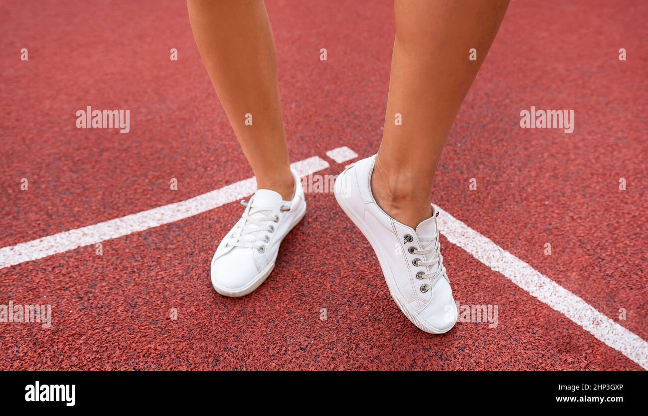 Rivestimento in plastica rossa sul parco giochi, le gambe di una ragazza in sneakers bianche. Preparazione al concorso Foto Stock
