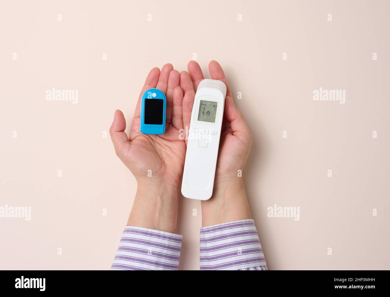 la mano femmina tiene il termometro in plastica senza contatto e l'ossimetro su sfondo beige Foto Stock