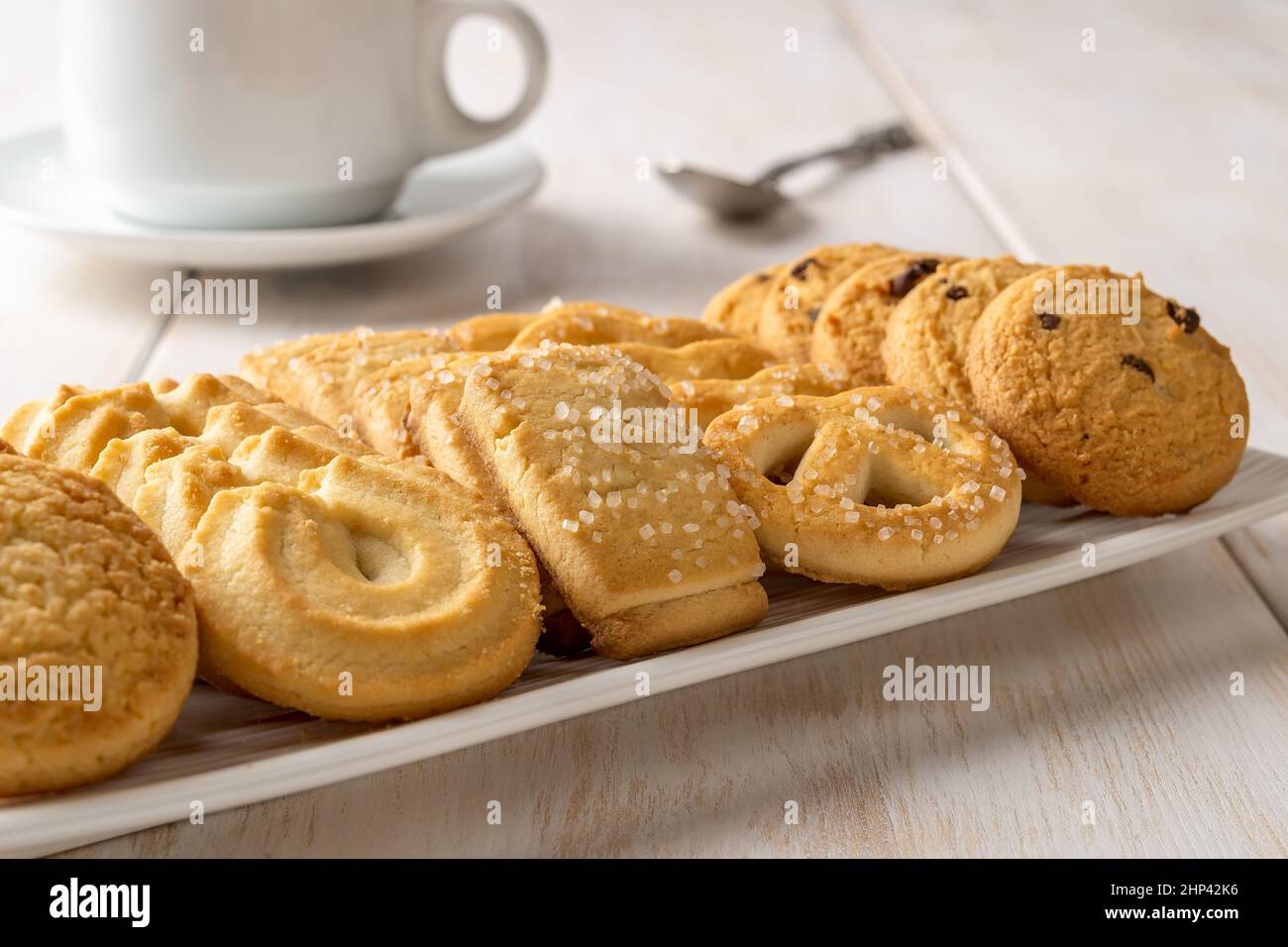 Set di biscotti danesi al burro su una piastra rettangolare bianca e una tazza di caffè. Biscotti frollini croccanti assortiti e primo piano con un teacup. Pasticceria al forno. Foto Stock
