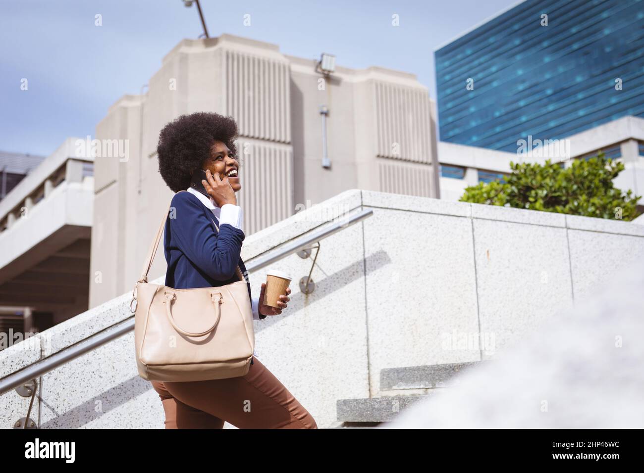 Felice afroamericana metà adulta donna d'affari parlare al telefono mentre si arrampicano i gradini in città Foto Stock