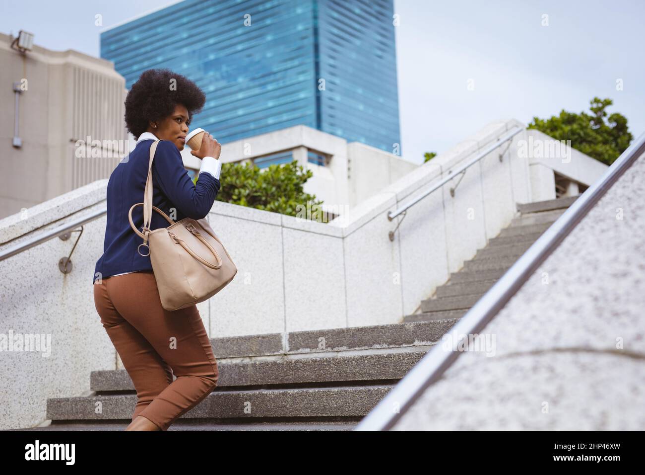 Donna d'affari afroamericana di metà adulto che ha un caffè mentre arrampica sui gradini in città Foto Stock