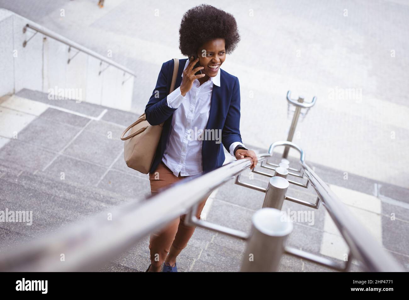 Sorridente uomo d'affari afroamericano adulto che parla al telefono mentre si arrampicano i gradini in città Foto Stock