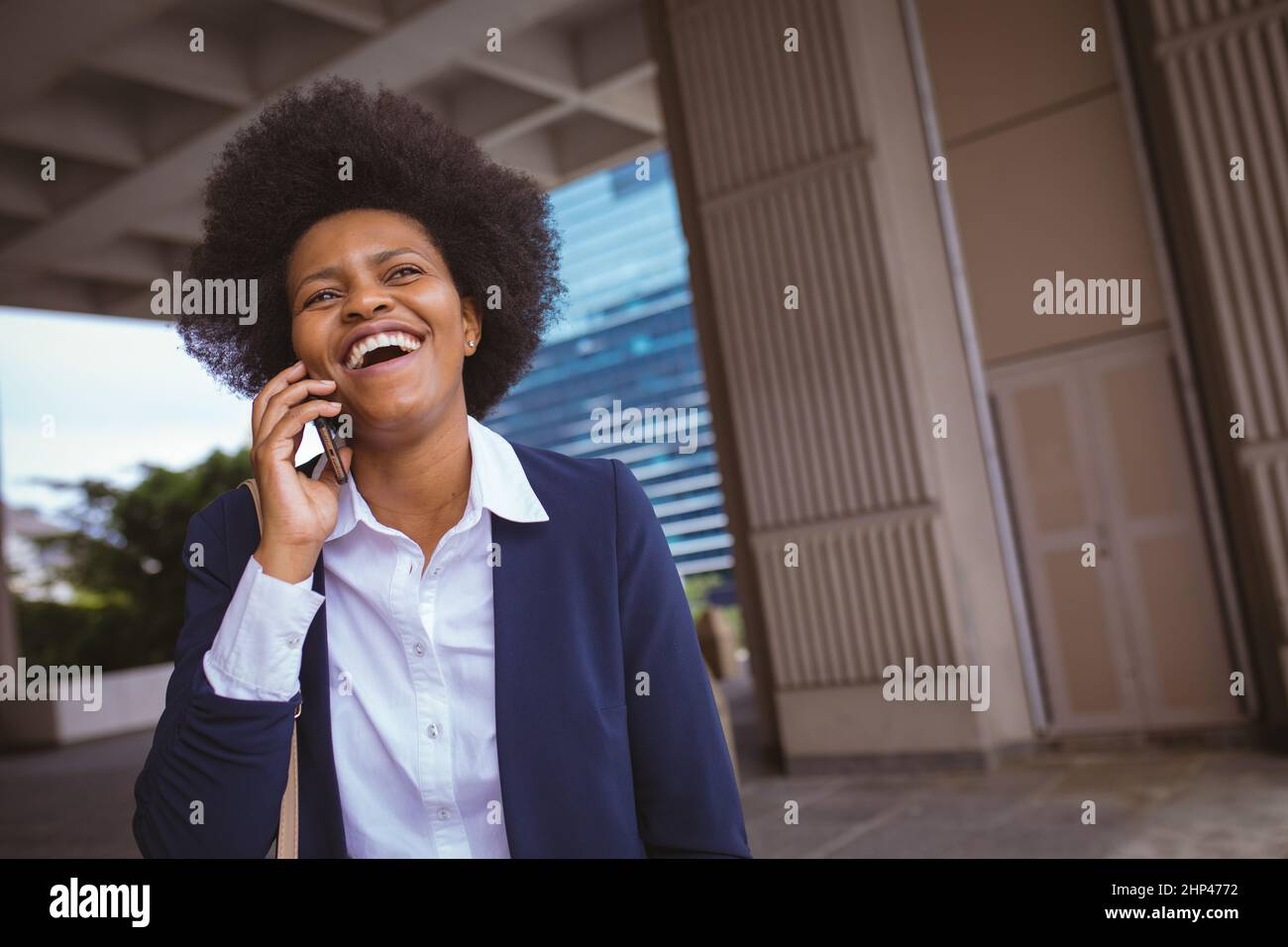 Felice afroamericana metà adulta donna d'affari parlare al telefono mentre in piedi in edifici Foto Stock