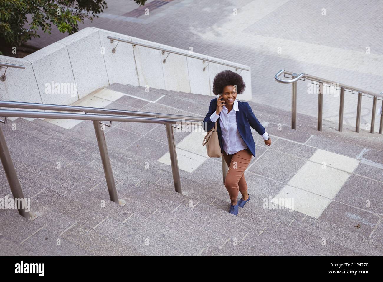 Felice afroamericana metà adulta donna d'affari parlare al telefono mentre si arrampicano i gradini in città Foto Stock