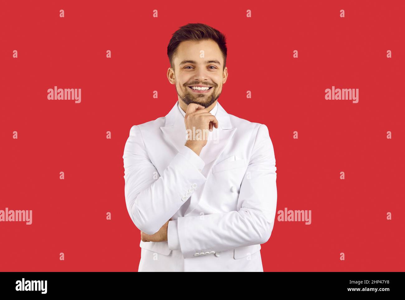 Felice bel giovane uomo alla moda in abito bianco isolato su sfondo rosso Foto Stock