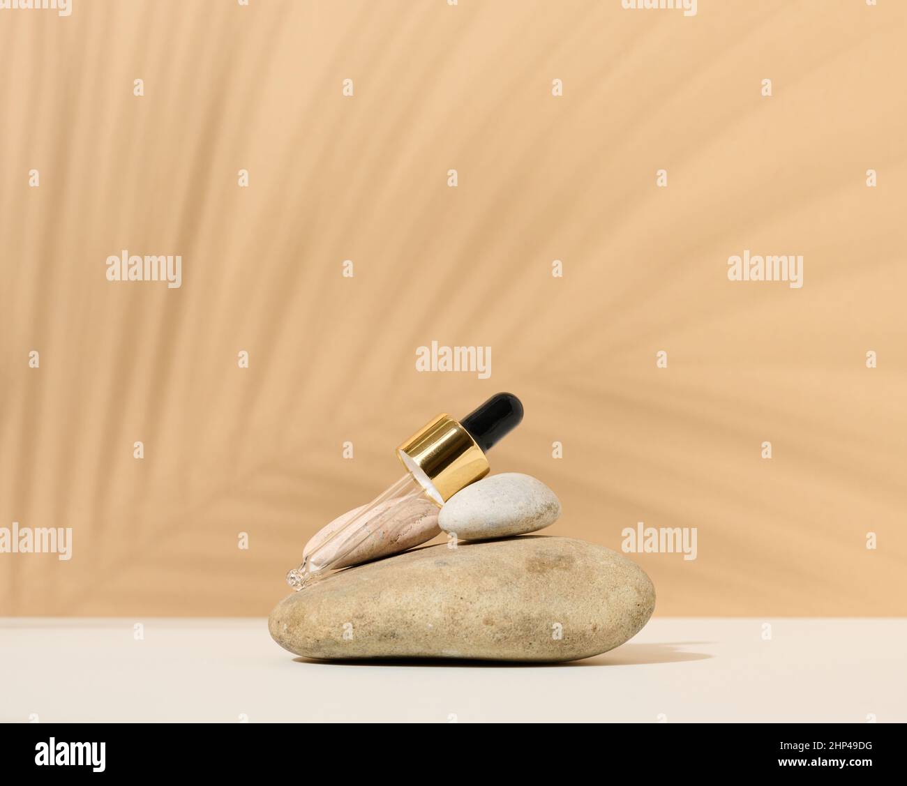 una pipetta di vetro per una bottiglia cosmetica si trova su una pila di pietre, l'ombra di una foglia di palma Foto Stock