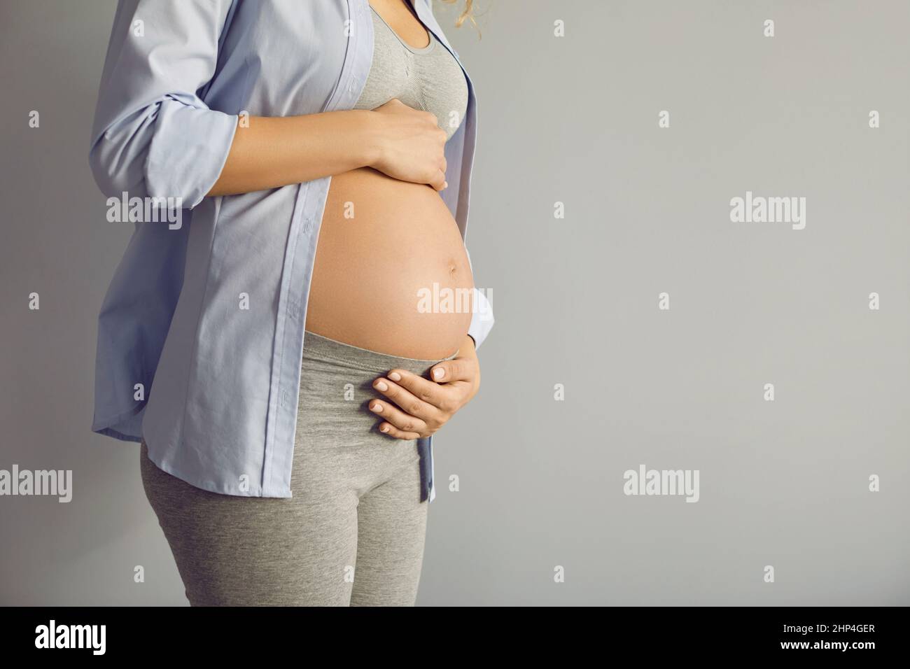 Primo piano di bella pancia di donna incinta al nono mese in piedi su sfondo grigio. Foto Stock