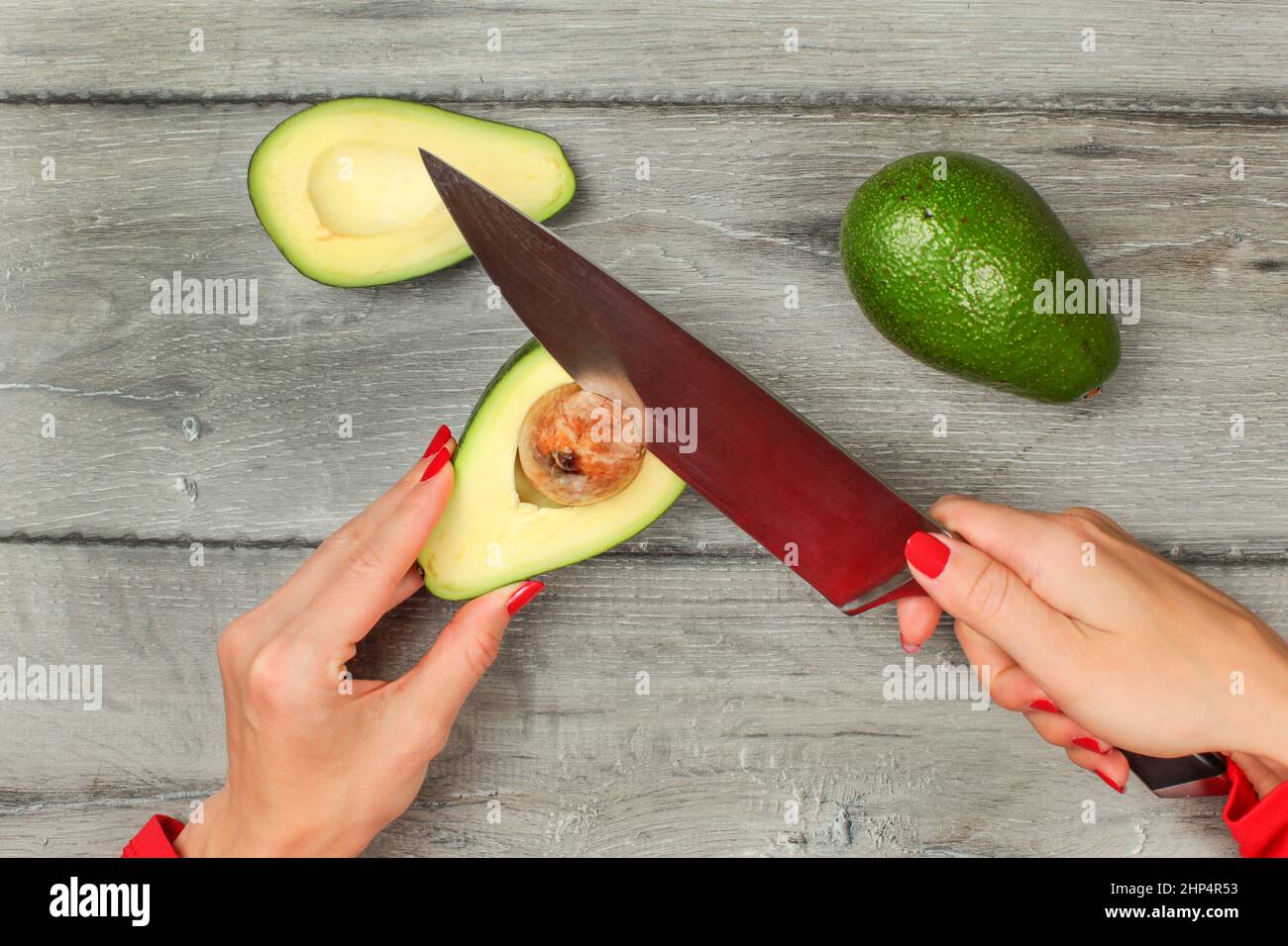 Tabella vista superiore, donna rimozione di seme di avocado con un coltello da chef. Foto Stock