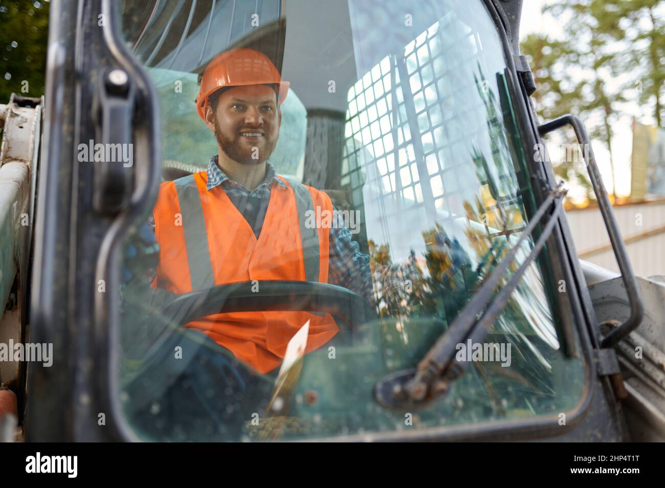 Sorridente operatore di costruzione che guida un veicolo seduto in cabina. Primo piano operatore attrezzature pesanti Foto Stock