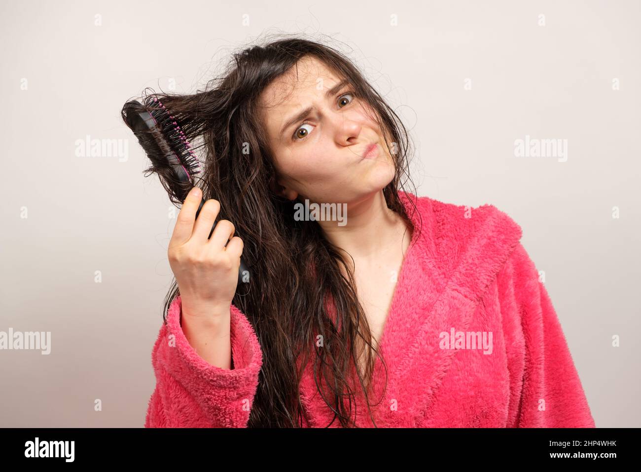 Una donna cerca di pettinare i capelli bagnati aggrovigliati. Cura dei capelli a casa, perdita dei capelli e sezione. Foto Stock