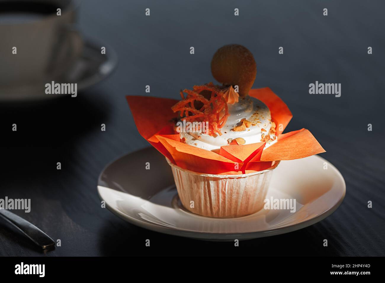 muffin in un pacchetto arancione, decorato con dolci e arachidi arancioni, si trova su un piatto di porcellana bianca su un tavolo nero, sullo sfondo di Foto Stock