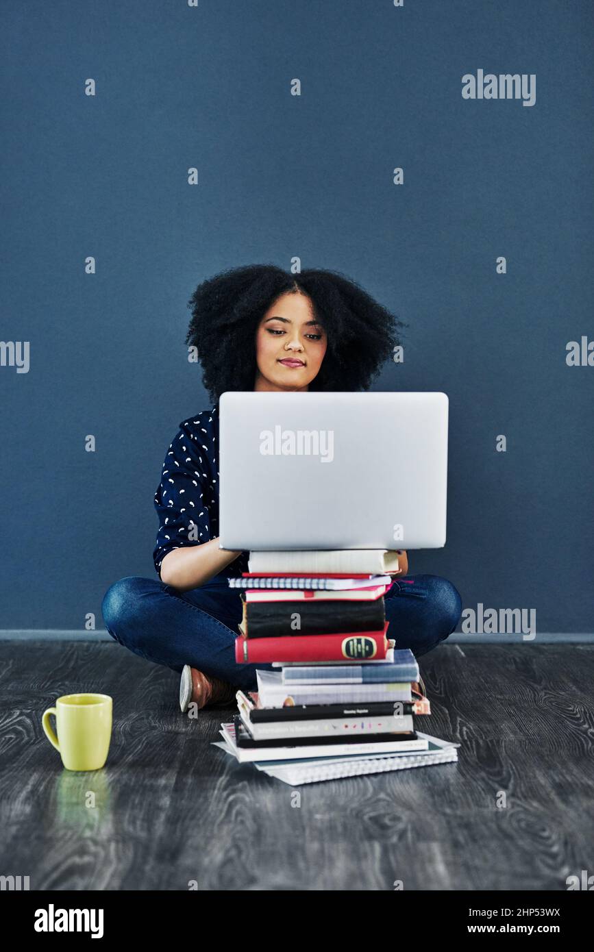 Cercate sempre le conoscenze. Studio girato di una giovane donna utilizzando un portatile con libri accatastati davanti a lei su uno sfondo blu. Foto Stock