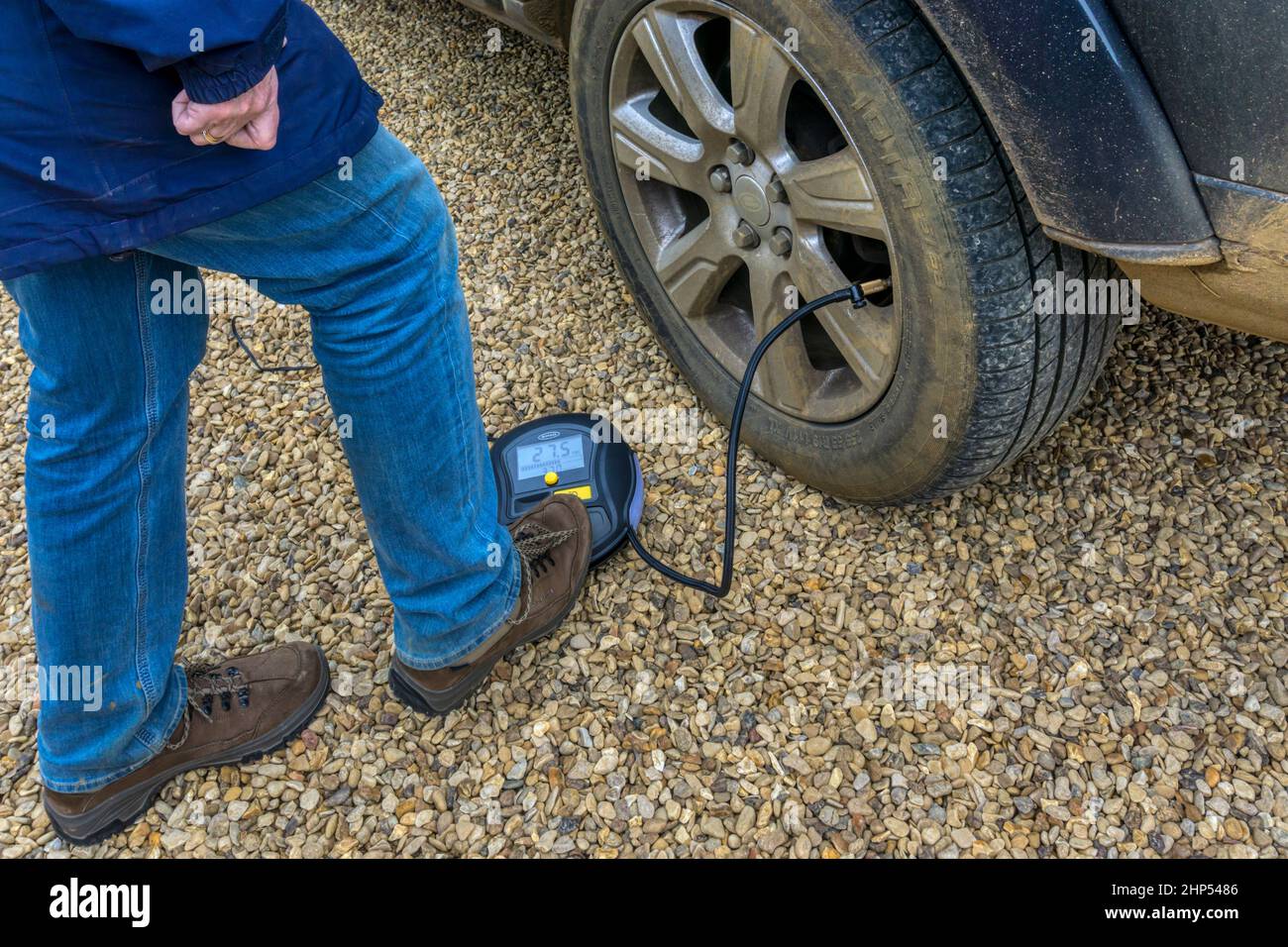 Donna che gonfia uno pneumatico su un SUV utilizzando un compressore d'aria portatile alimentato dalla batteria dell'auto. Foto Stock