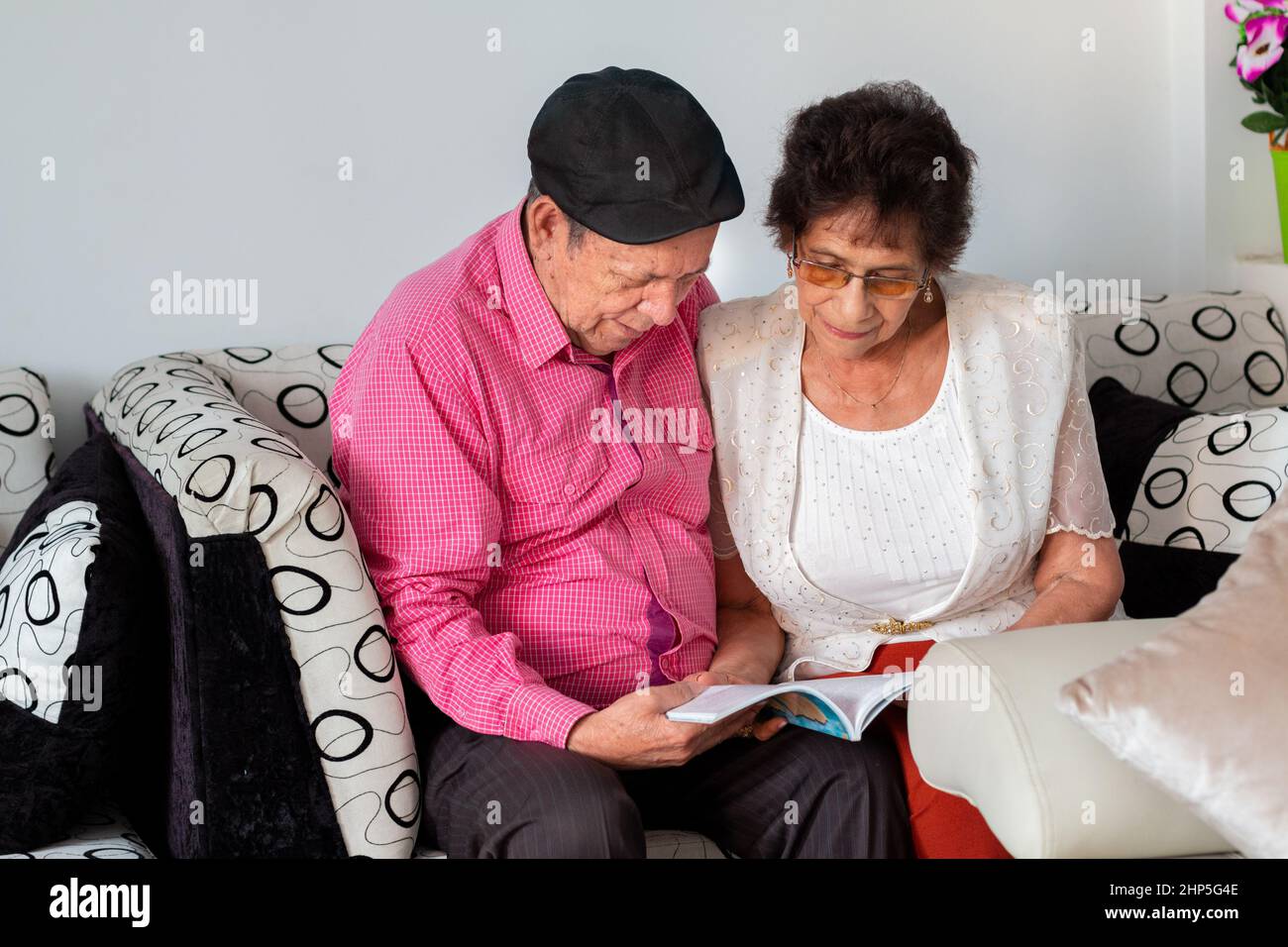 Coppia anziana seduta su un divano lettura di un libro insieme nella comodità della loro casa. Foto Stock