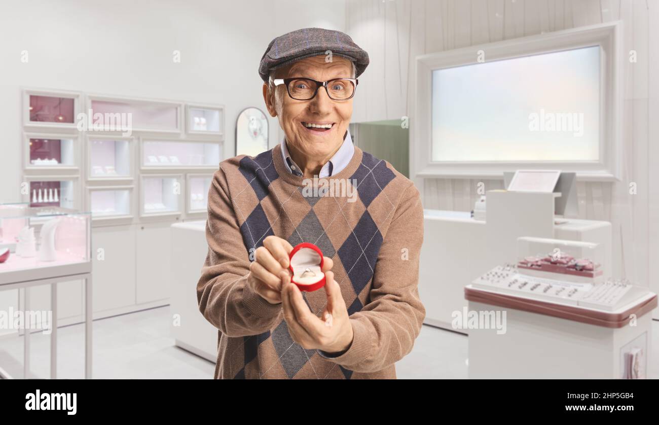 Uomo anziano felice che tiene un anello in una scatola all'interno di un negozio di gioielli Foto Stock