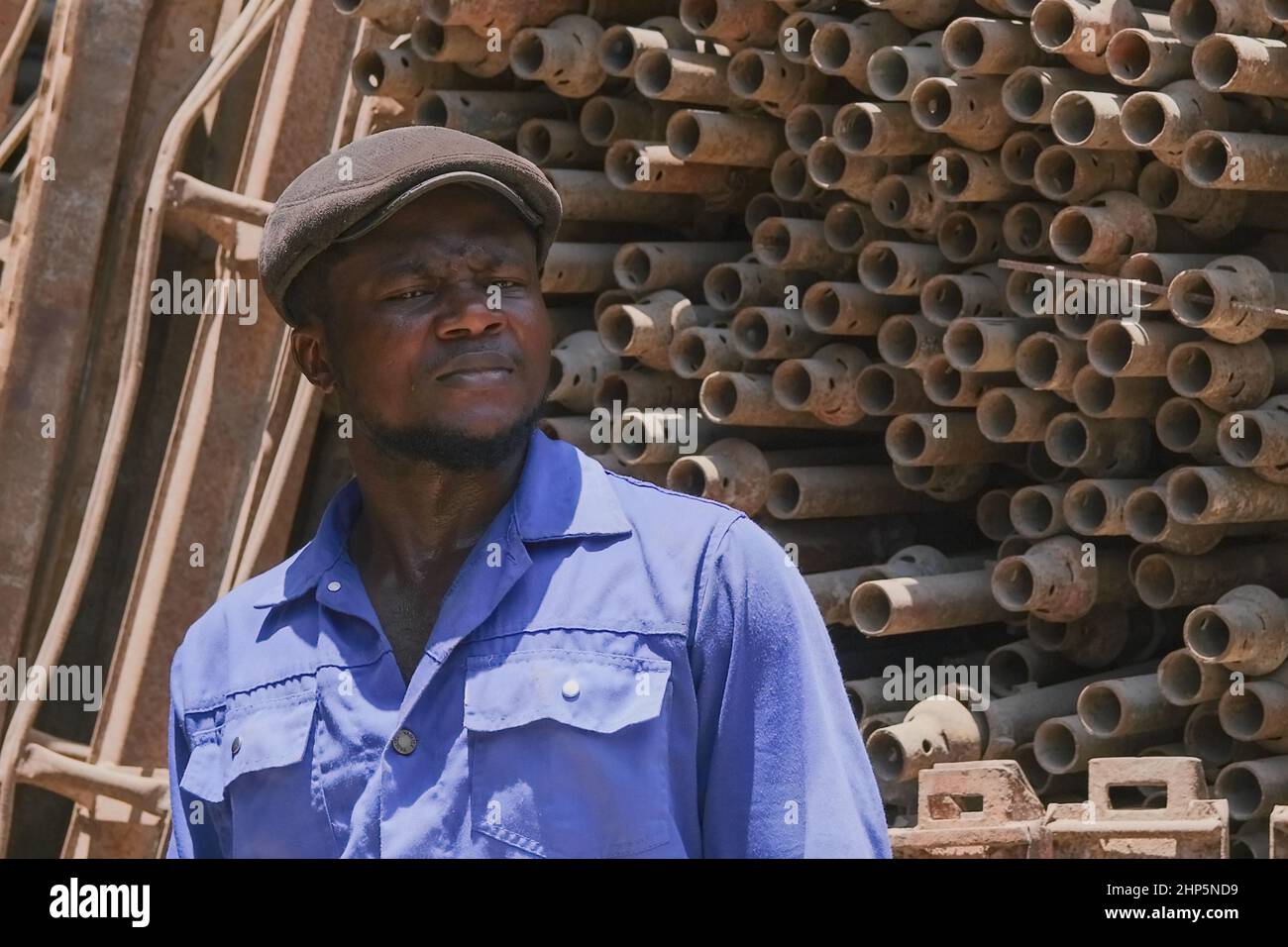 Fuoco selettivo di fronte al nero africano uomo operaio indossando uniforme blu, lavorando per rottame metallo magazzino di approvvigionamento per il riciclaggio. Abu Dhabi, Emirati Arabi Uniti Foto Stock