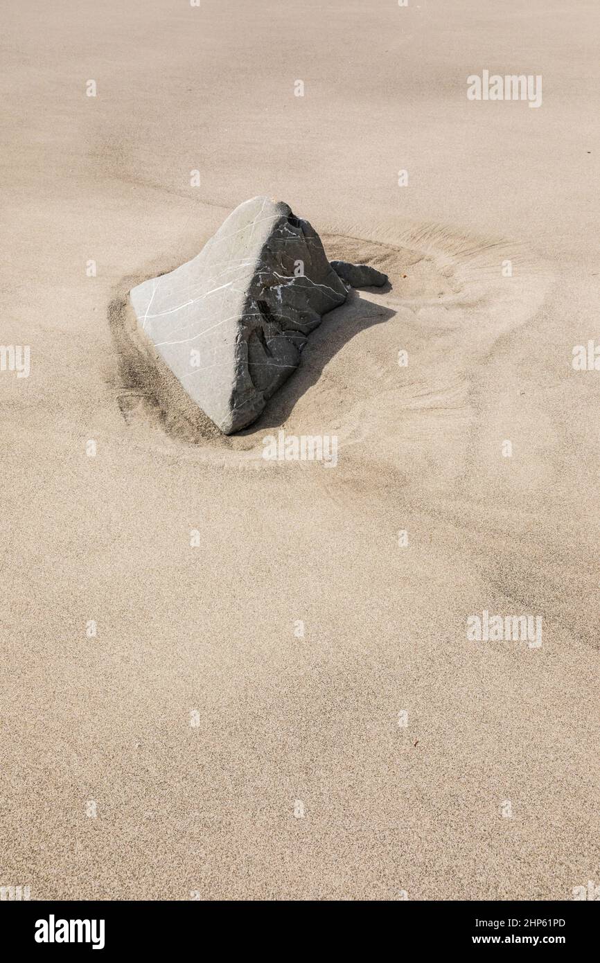 Una roccia esposta sopra una spiaggia sabbiosa dopo che le maree si sono calate. Foto Stock