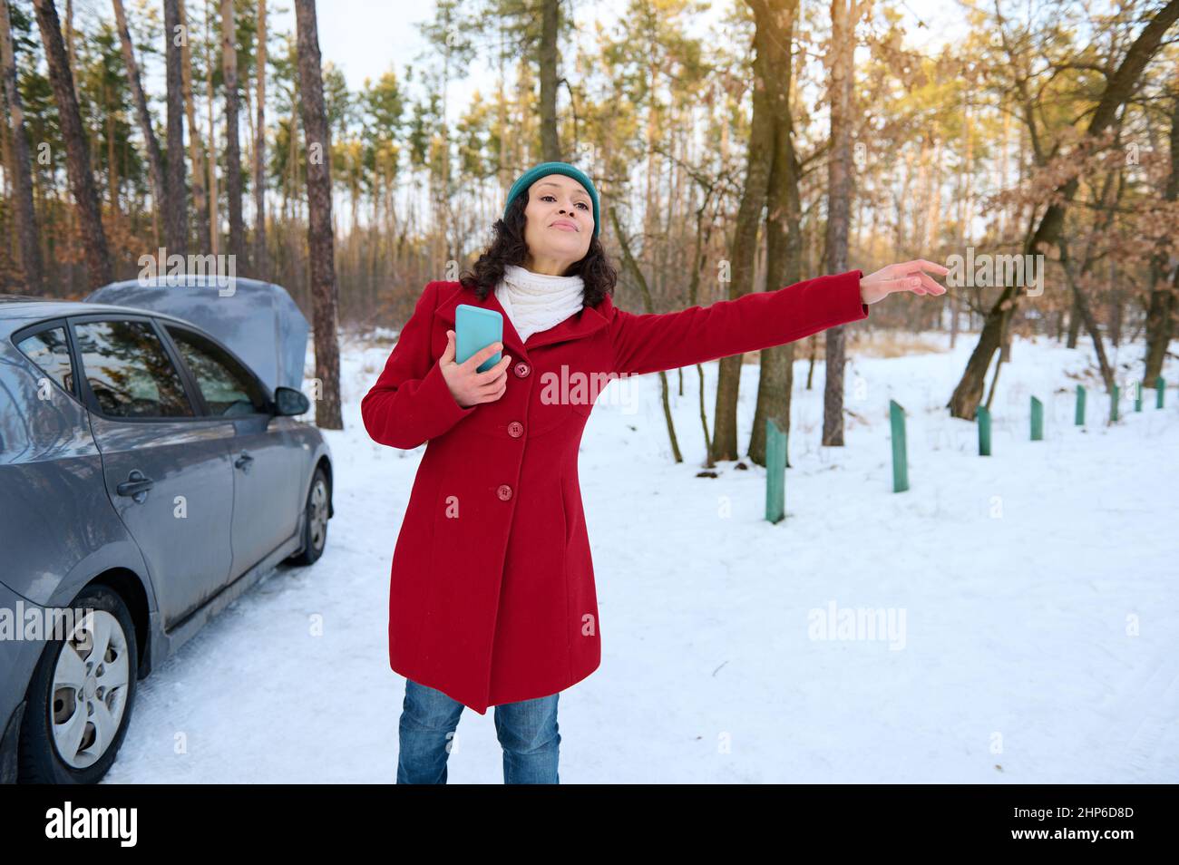 Frustrata stordita conducente donna che tiene un telefono cellulare mentre cerca di trovare aiuto durante un guasto auto. Dispositivo di frenatura automatico. Guasto auto, auto Foto Stock