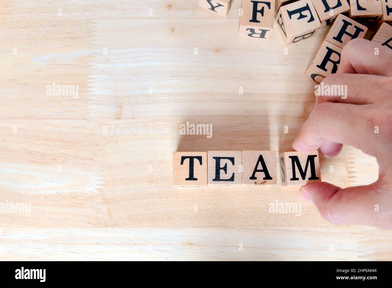 Idea di concetto di squadra, primo piano su mano destra che raccoglie le lettere di legno si collegano al messaggio sulla scrivania di legno, informativo e comunicazione circa il lavoro di squadra per il team Foto Stock
