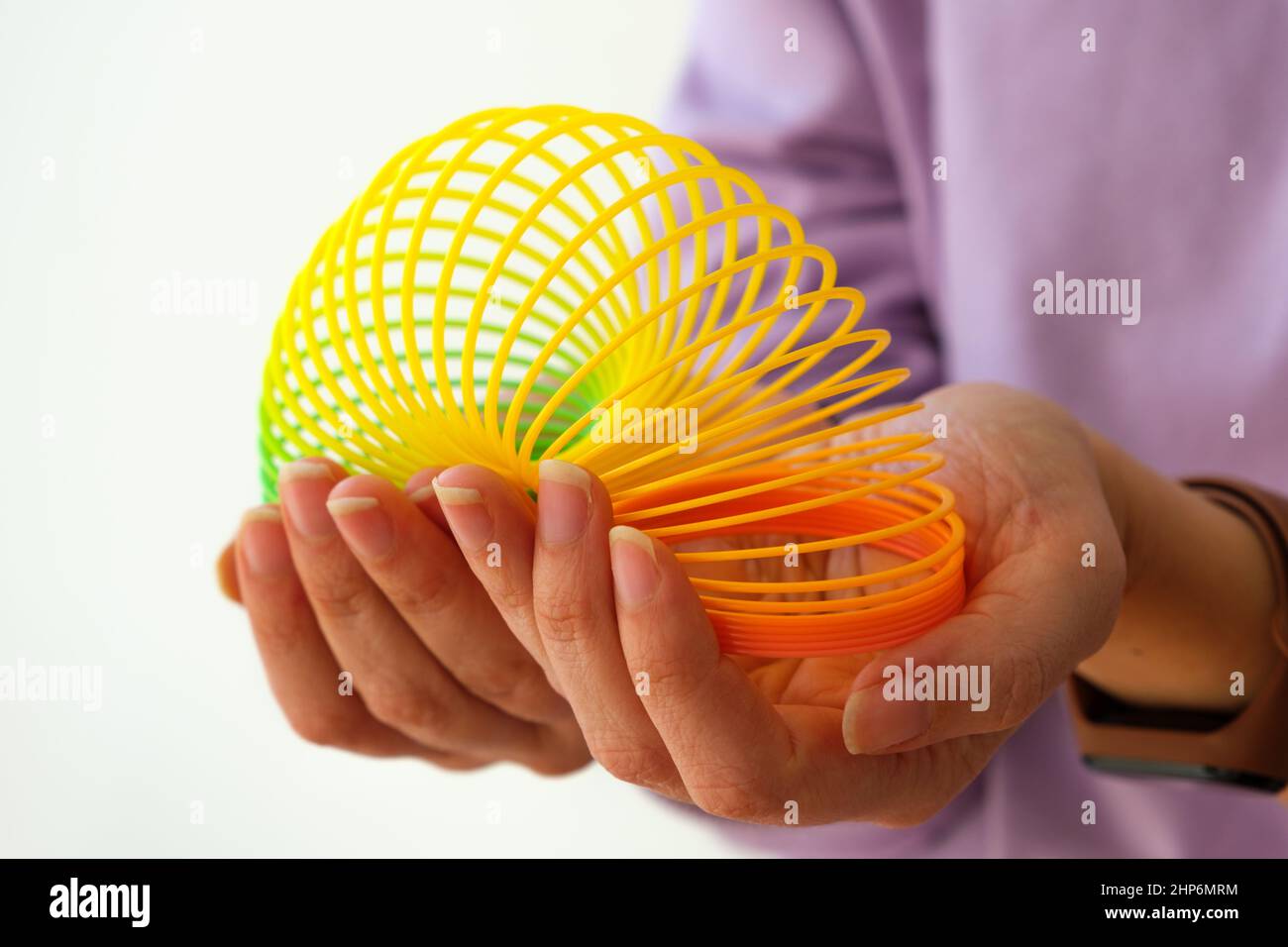 Donna che gioca con il giocattolo magico della molla degli anni novanta, arcobaleno allungabile in plastica in mano per alleviare o ridurre lo stress su sfondo bianco. Foto Stock