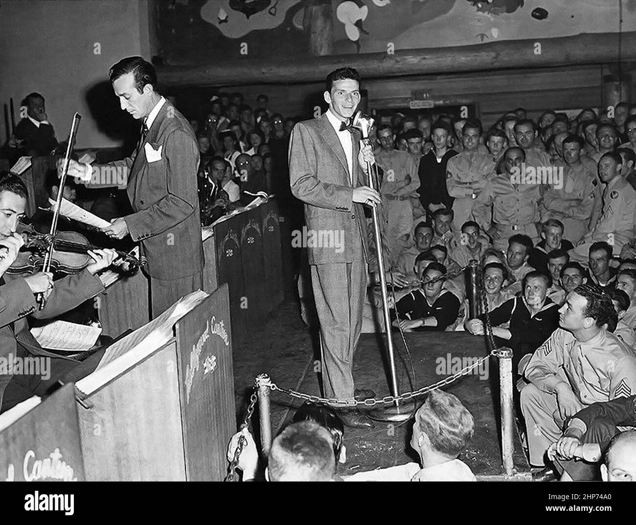 Foto pubblicitaria di Frank Sinatra (centro) che si esibisce presso la mensa di Hollywood per i militari statunitensi durante la seconda Guerra Mondiale, accompagnato da Harry James (a sinistra, in piedi con spartiti musicali) e la sua grande band ca. 1943 Foto Stock