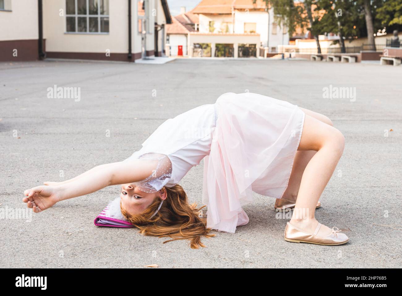 Piccola ragazza zenzero in abito rosa che fa posa ponte Foto Stock