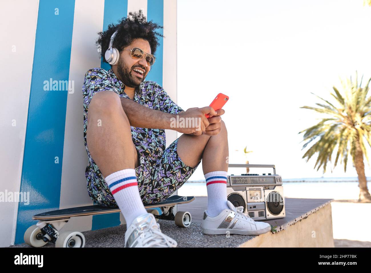 Uomo ispanico divertirsi con smartphone mobile e ascoltare musica in spiaggia tropicale Foto Stock