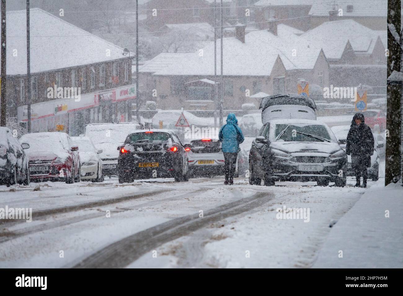Neve e ghiaccio che causano disagi sulle colline intorno a Bradford, West Yorkshire, Regno Unito. 19th Feb 2022. Le auto lottano per muoversi su superfici invernali scivolose. Le donne cercano di liberare le ruote su una collina nevosa per far muovere la loro auto. Foto Stock