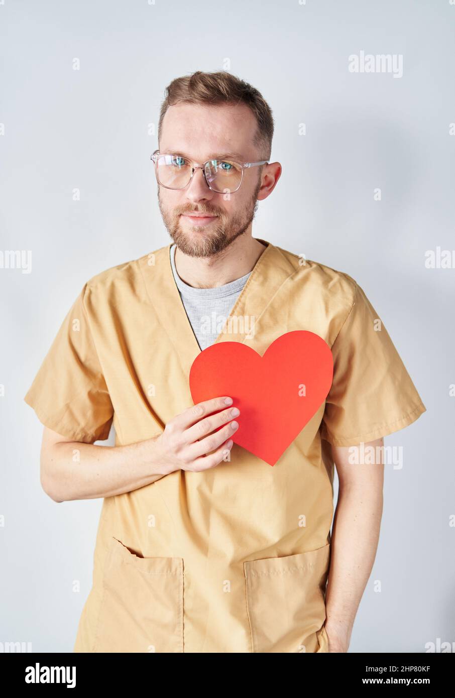 Medico cardiologo maschile caucasico in uniforme medica e occhiali con forma di cuore di carta rossa. Medico chirurgo adulto che posa in ospedale. Concetto di Giornata Nazionale dei Medici. Immagine di alta qualità Foto Stock