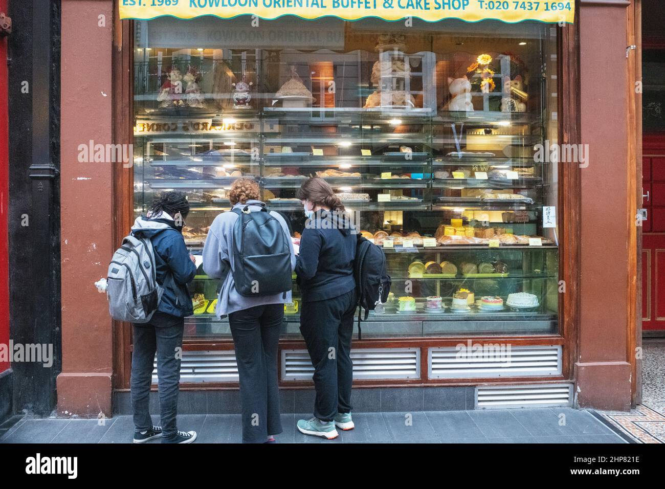 Tre giovani che guardano alla finestra dell'Oriental Kowloon buffet and Cake Shop, Gerrard Street, Chinatown, Londra Foto Stock