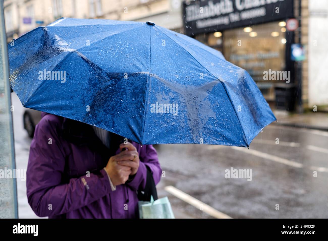 Una donna shopper ripara sotto il suo ombrello, su una città High Street, come la pioggia pesante cade durante il tempo inclemente come Storm Eunice colpito il sud-ovest del regno unito Foto Stock