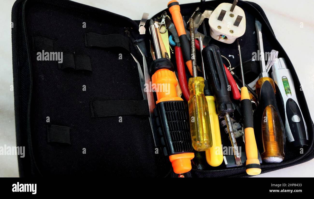 Primo piano di una borsa portautensili con utensili non ordinati di pinzette, cacciaviti, pinze, spina a 3 pin e altri. Foto Stock