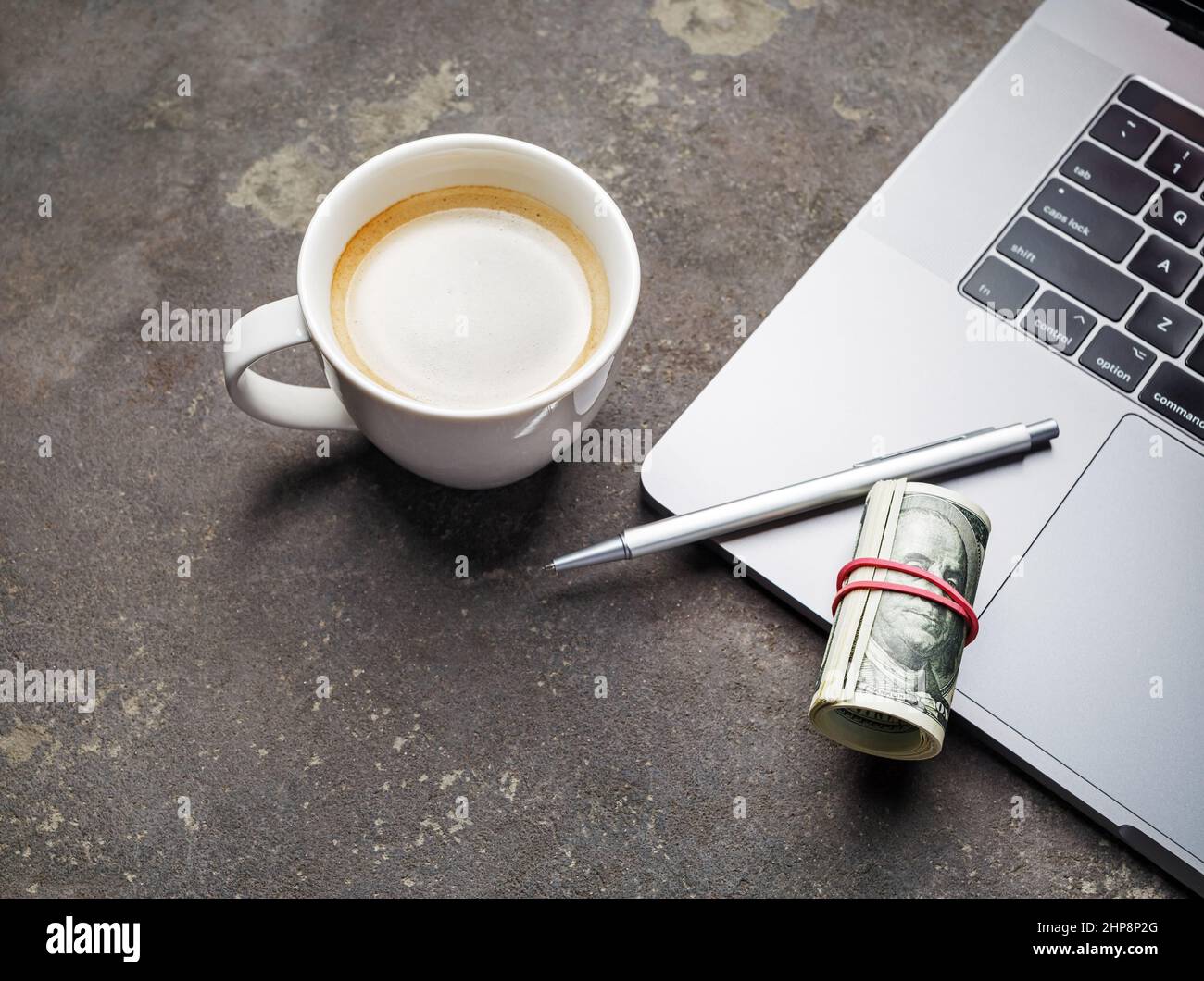 Concetto di business online. Denaro, penna, tazza da caffè e tastiera per computer portatile su sfondo in cemento. Foto Stock