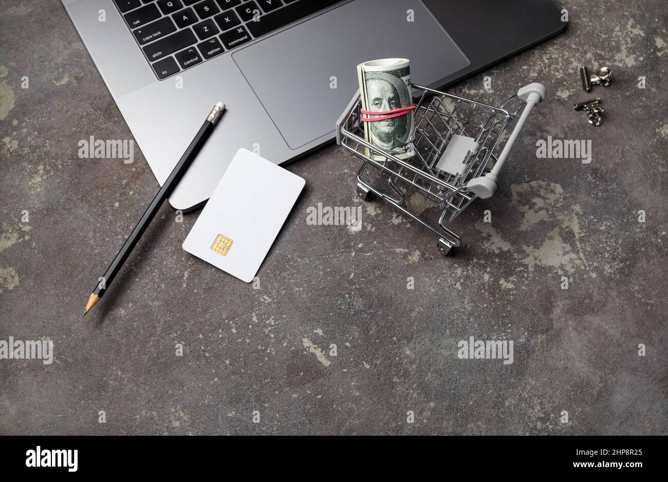 Concetto di shopping online. Soldi, carrello della spesa, carta di credito, matita e tastiera del laptop su sfondo concreto. Foto Stock