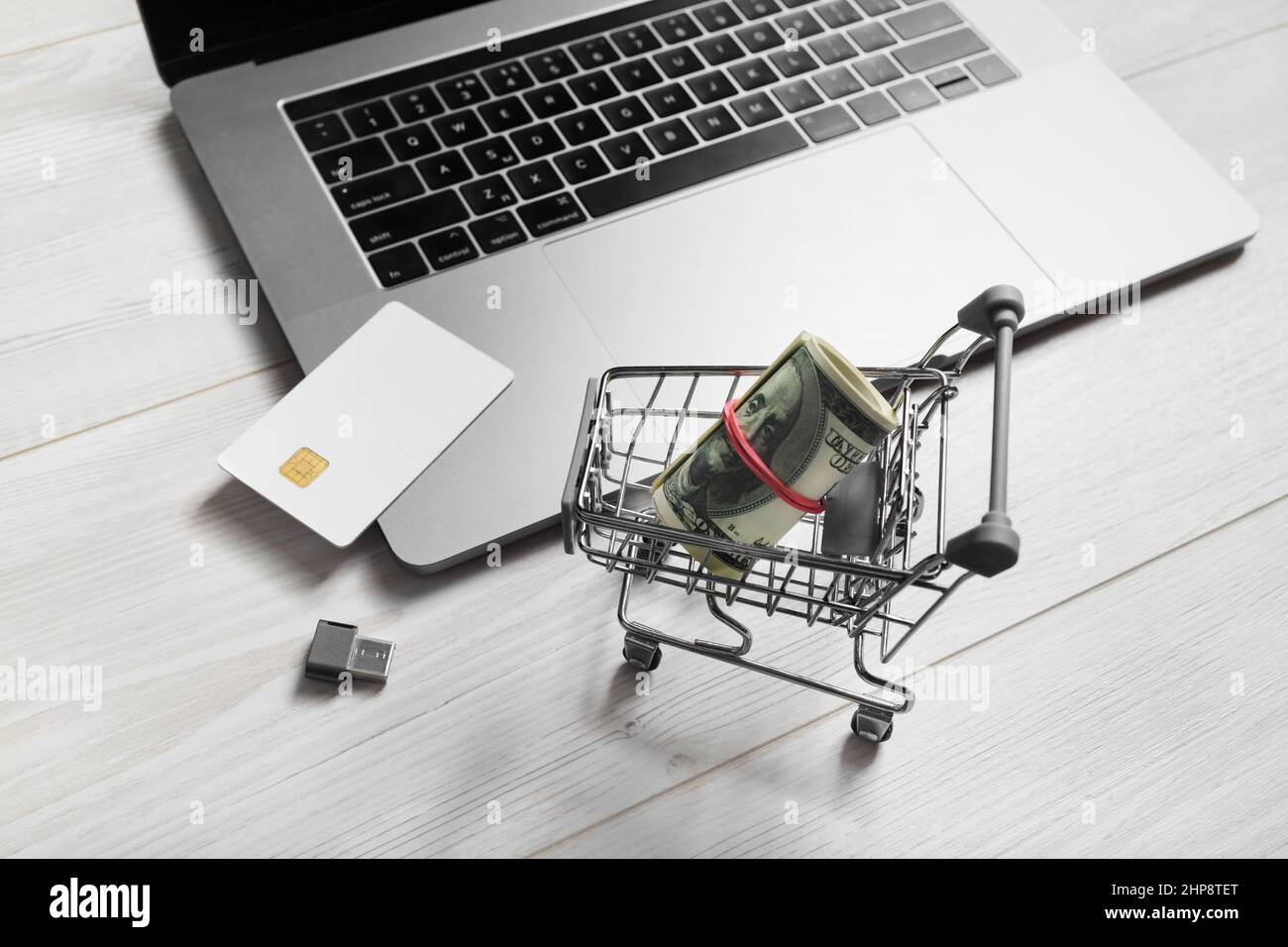 Concetto di shopping online. Computer portatile, carrello per lo shopping, carta di credito, denaro e unità flash usb su sfondo di legno chiaro Foto Stock