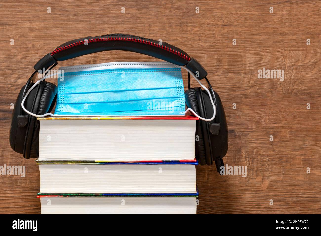 Libri, cuffie, maschera su sfondo di legno. Maschera protettiva e libri. Concetto di autoisolamento, QUARANTENA, PANDEMIA, CORONAVIRUS, audiolibro Foto Stock