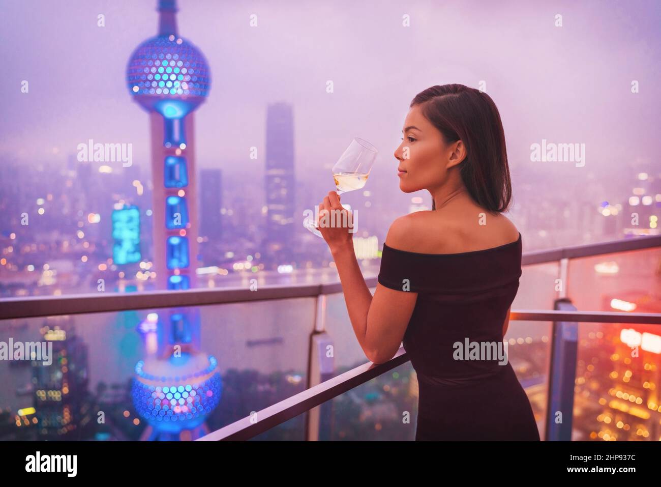 Lusso Shanghai stile di vita asiatica donna bere vino bianco in su China Travel. Modello elegante in abito nero su terrazza vista della città, di alta classe Foto Stock