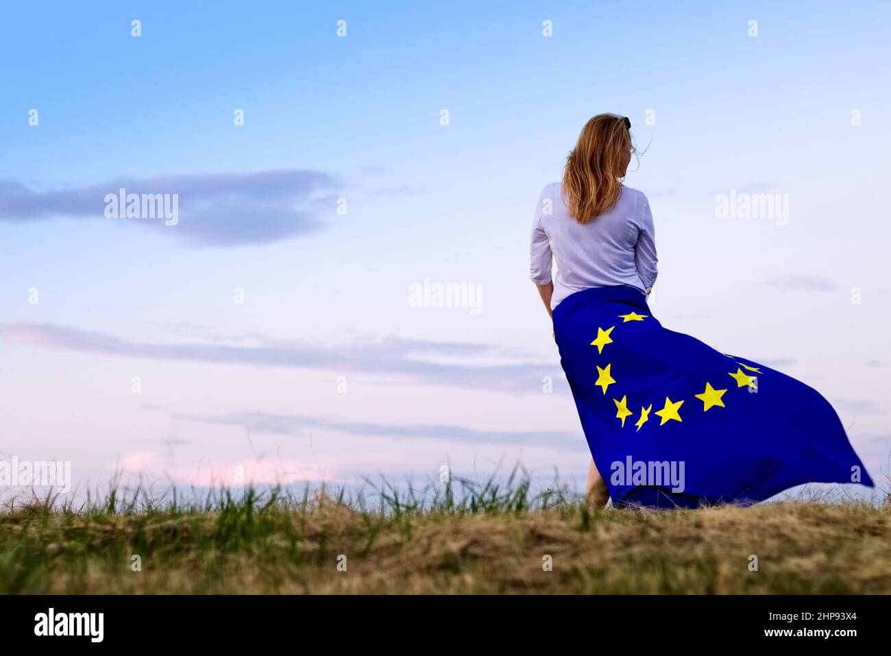 Donna con bandiera dell'Unione europea all'orizzonte in natura. I capelli biondi indossano la bandiera UE come gonna Foto Stock