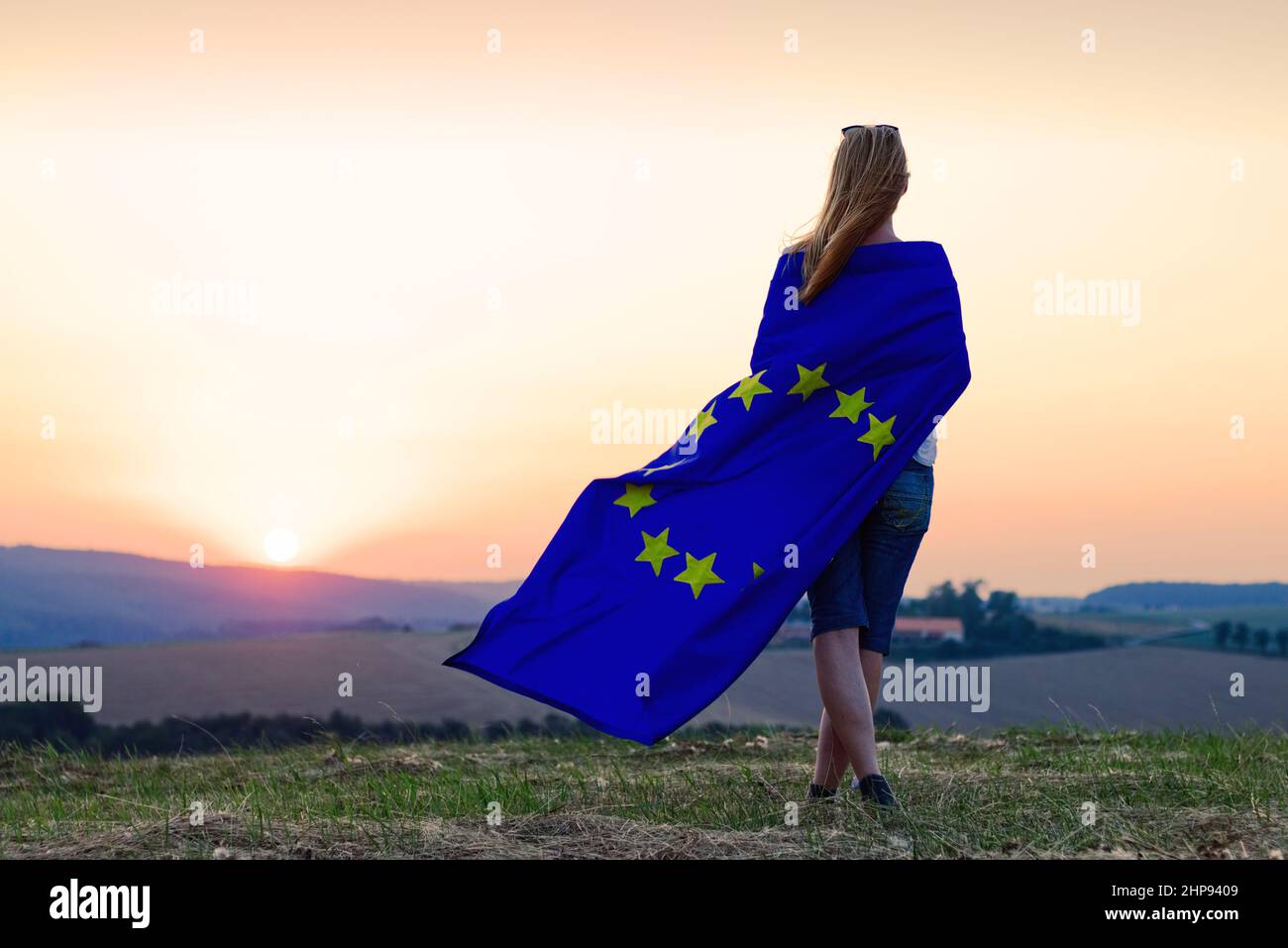Crepuscolo sull'Unione europea. Donna che batte bandiera dell'Unione europea e guarda il tramonto Foto Stock