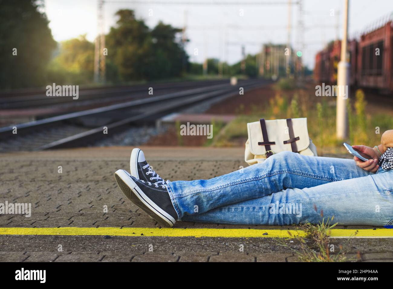 La donna turistica è seduta sulla piattaforma della stazione ferroviaria e in attesa di un treno. Backpacker indossando jeans e sneaker Foto Stock