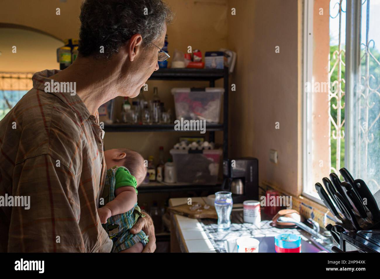 Un più anziano expat tiene il suo figlio nato in Nicaragua mentre guarda attraverso una finestra a Managua, Nicaragua Foto Stock