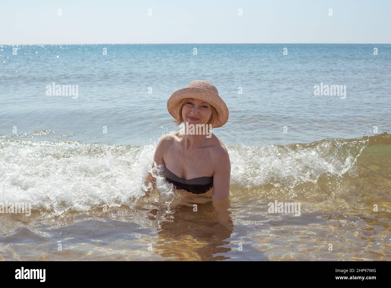 Bella donna in cappello e bikini in acqua di mare sorridente. Passatempo estivo e relax. Foto Stock