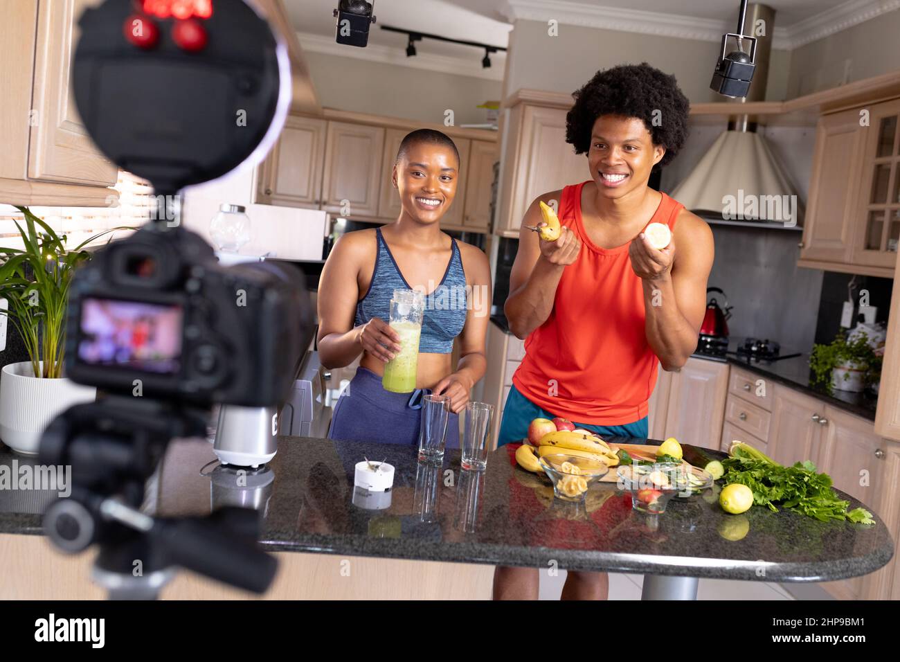 Sorridendo giovani influencer biraciali mostrando cibo e bevande sani alla macchina fotografica vlogging in cucina Foto Stock
